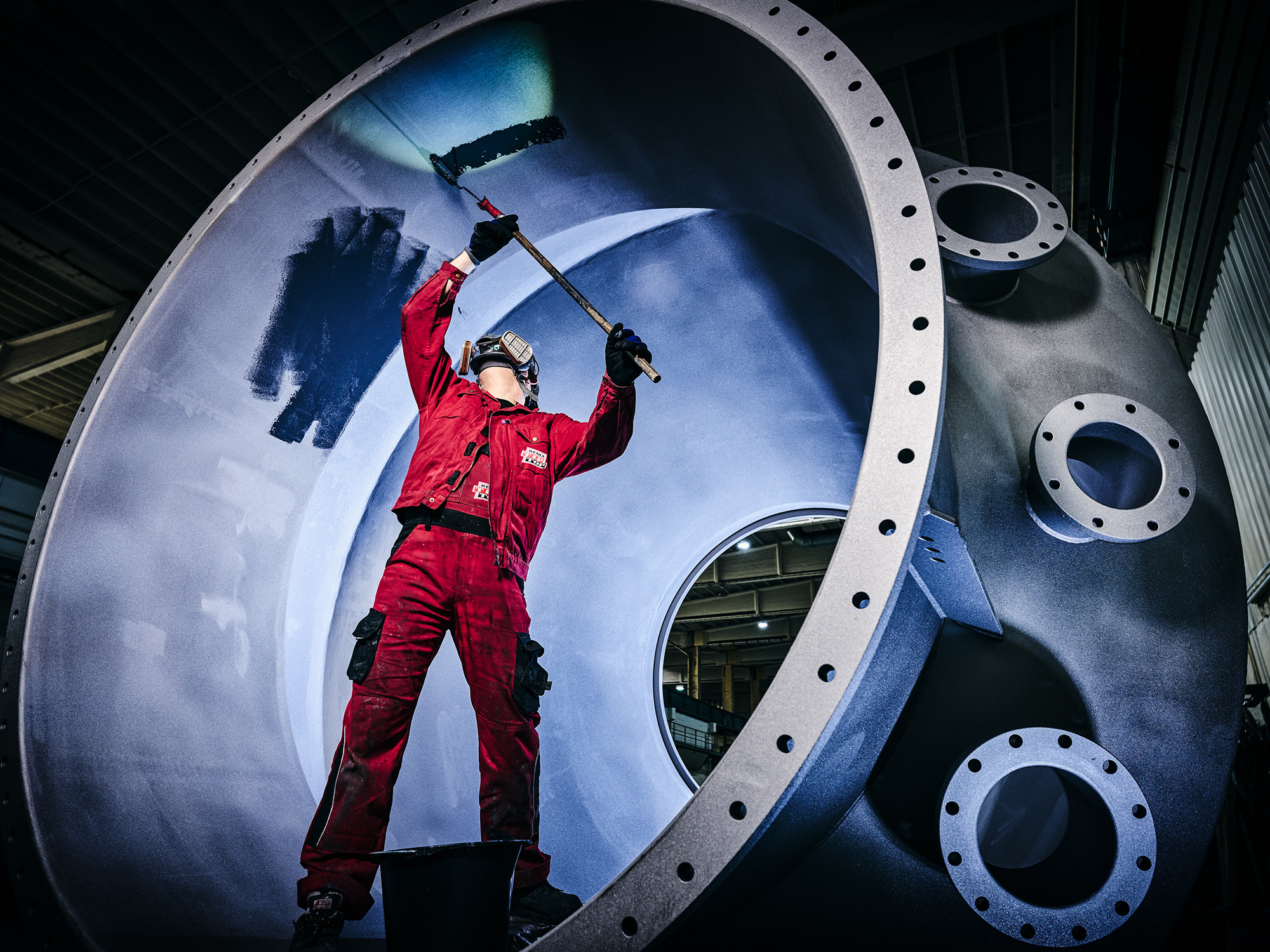Mitarbeiter trägt Korrosionsschutzbeschichtung im Inneren eines großen Industriebehälters mit einer Farbrolle auf